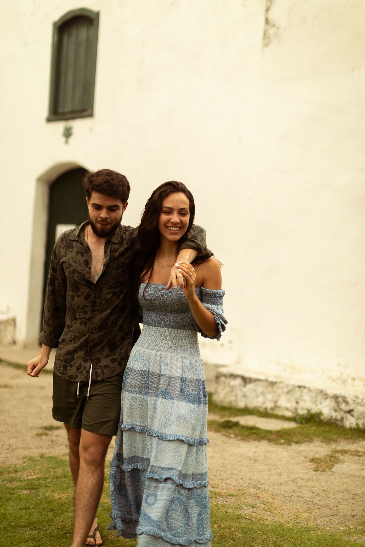 A couple walking together in a casual outdoor setting wearing summer clothing and embracing while walking.