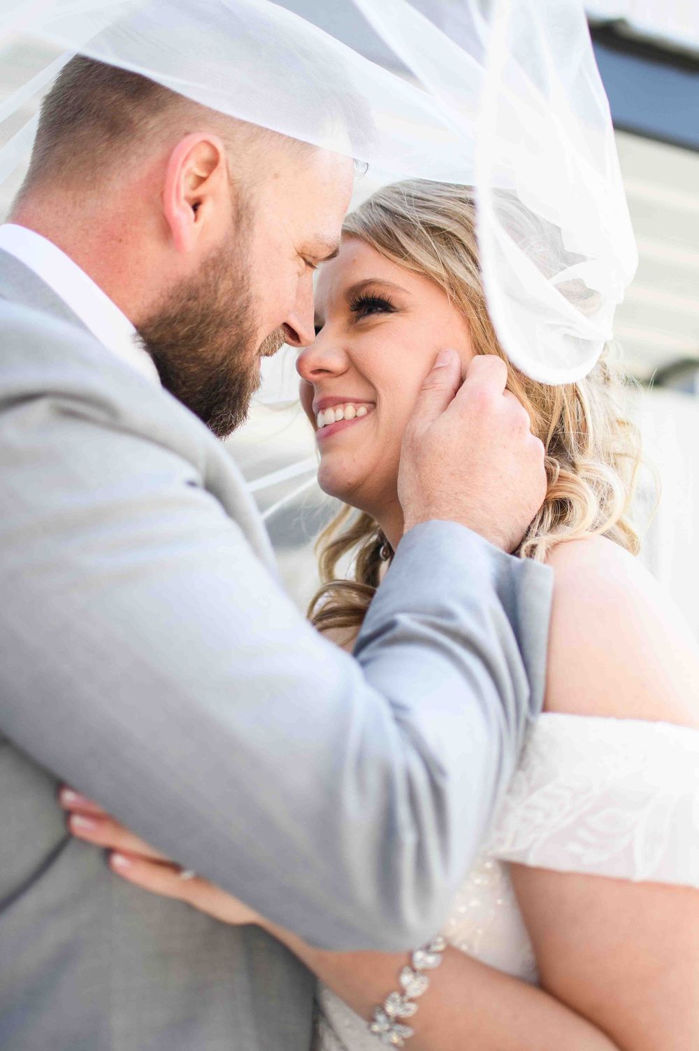 Bride and groom embrace under softly lit, wedding veil blowing in the wind.