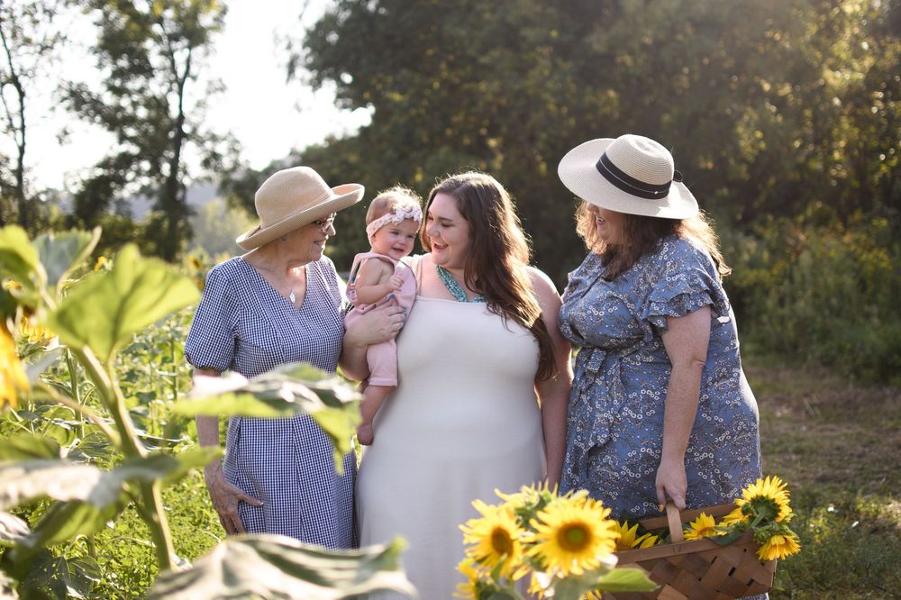 Multigenerational family portrait, with grandmother, mother, sister and daughter in a sunflower field at sunset.