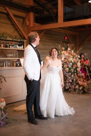 A couple shares their first dance in a rustic barn venue decorated with pink and white floral arrangements.