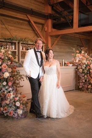 Wedding couple poses in rustic venue with elegant floral arrangements and romantic lighting.