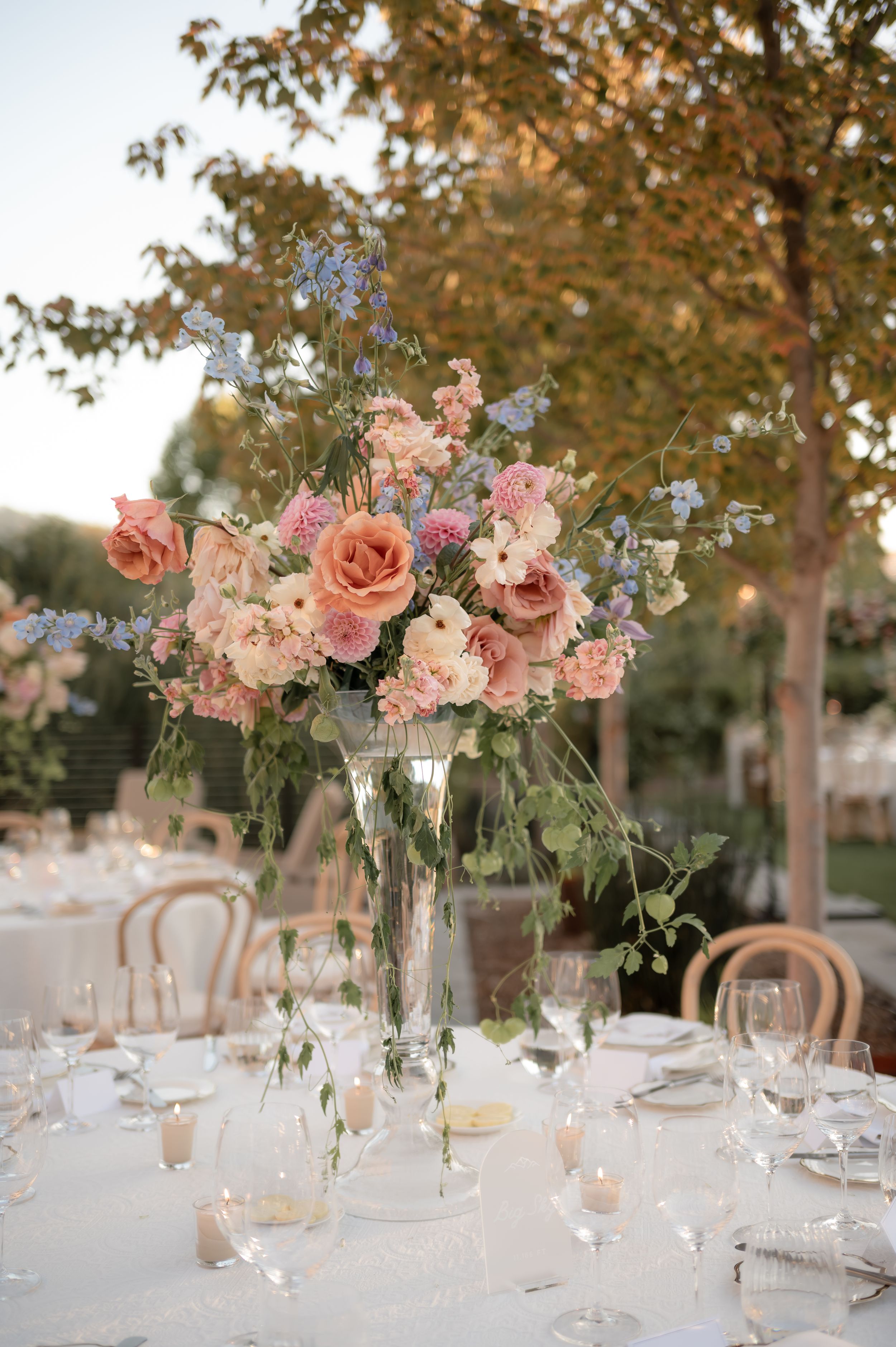 Elegant wedding table centerpieces featuring pink roses and greenery in crystal vases with soft candlelight.