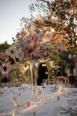 Elegant floral centerpieces with white and pink flowers in glass vases adorn tables at an outdoor sunset reception.