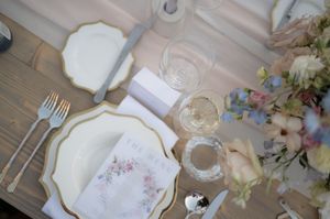 Elegant place setting with floral china plates, wine glasses and delicate flowers on a wooden table.