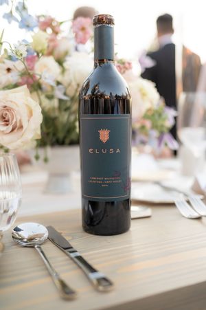 Elegant table setting with soft pink floral arrangements and dark blue wine bottles at an upscale event.