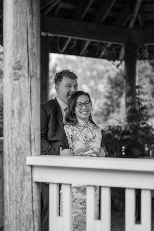 Black and white photograph of a couple sharing a joyful moment together on a porch with wooden columns.