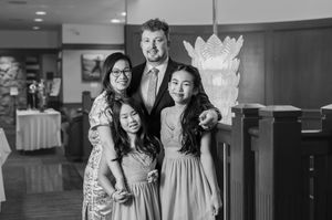 A black and white photograph of a family group posing together in an elegant indoor venue with decorative lighting.