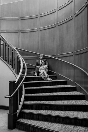 A person sits on an elegant curved staircase with wooden steps and metal railings in a black and white composition.