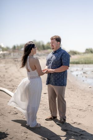 A couple shares a joyful moment together on a sunny beach, dancing and laughing in casual attire.
