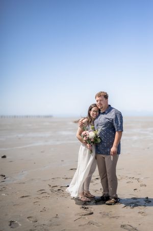 A couple shares a romantic moment on a misty beach with the bride holding a floral bouquet.