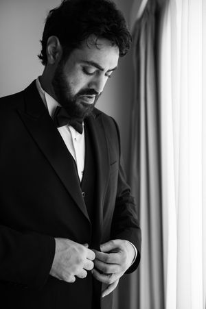 Black and white photo of someone in a suit adjusting their cuff link by a window.