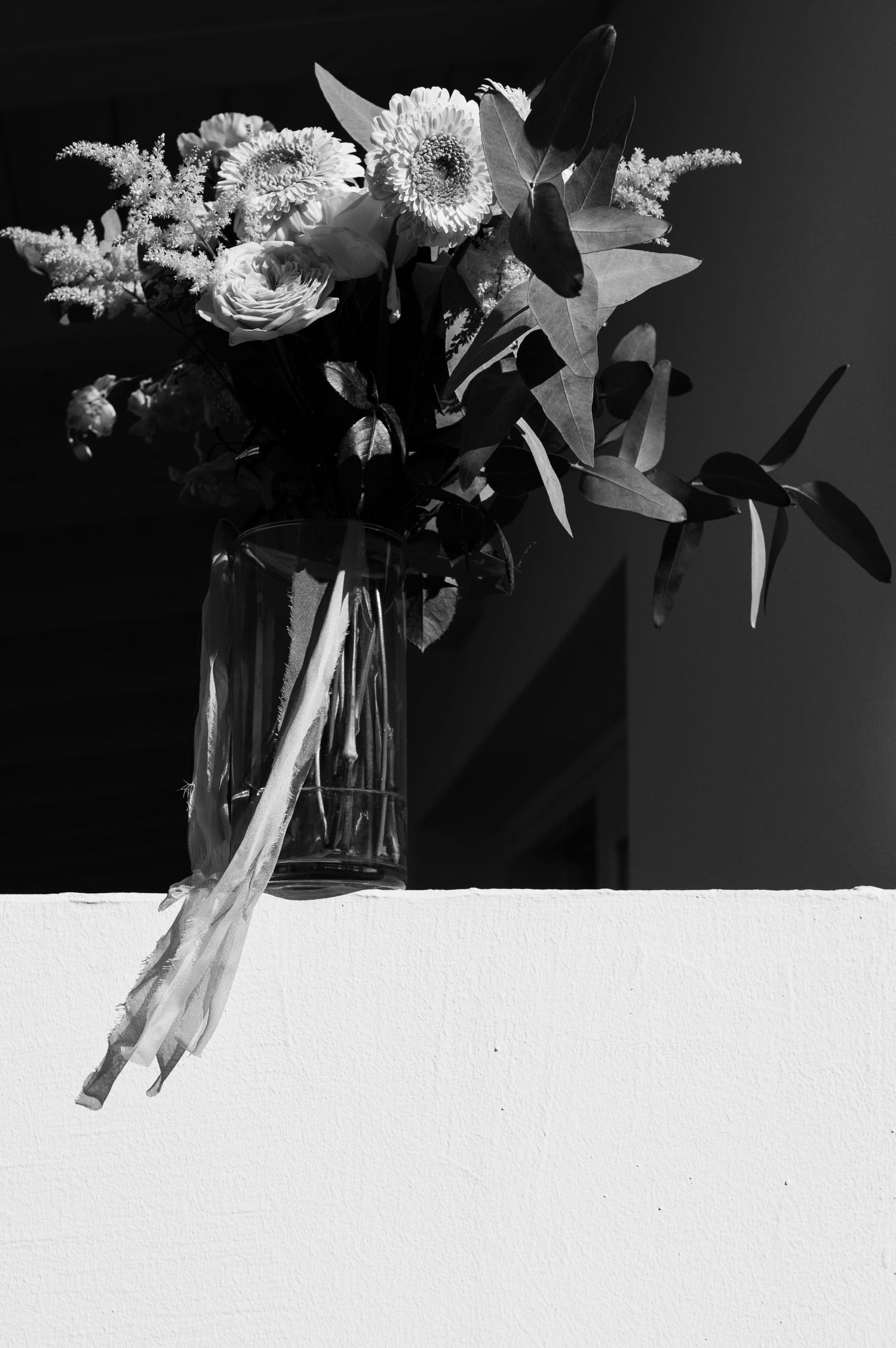 Black and white photograph of white chrysanthemums and lilies arranged in a glass vase against a dark background.
