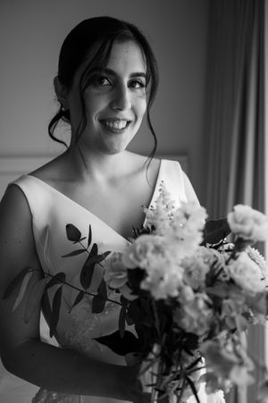 Black and white portrait of bride holding elegant white floral bouquet against soft window light.