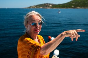 Smiling senior woman with sunglasses pointing over blue ocean waters on a sunny day.