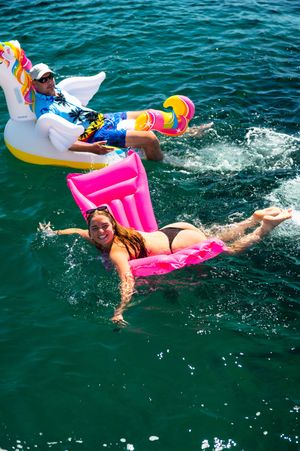 Two people enjoying summer on colorful inflatable floats in turquoise water, one on a unicorn and one on a pink raft.