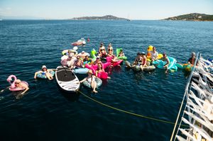 Group of people floating on colorful inflatables in calm blue sea water near a boat on a sunny day.