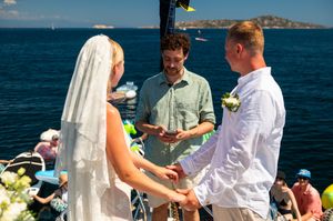 Couple exchanging vows at outdoor beach wedding ceremony on a boat with ocean backdrop on sunny day.