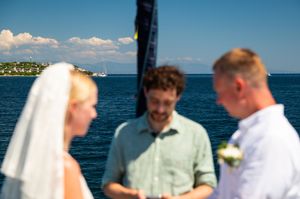 Outdoor wedding ceremony by the sea with bride, groom, and officiant under a blue sky.