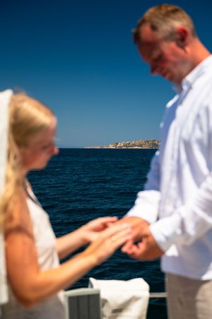 Bride placing wedding ring on groom's finger during outdoor ceremony on a boat with ocean backdrop.