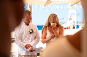 Emotional bride and groom exchanging vows at an outdoor beach wedding ceremony on a sunny day.