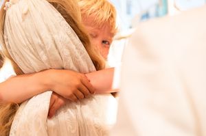 Young child in formal wear hugging bride in white wedding dress during wedding celebration.