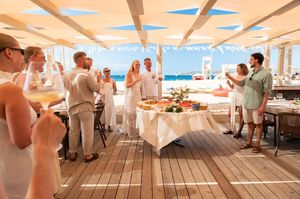 Guests celebrate at a beachside wedding reception under a pergola with ocean views and elegant white table settings.