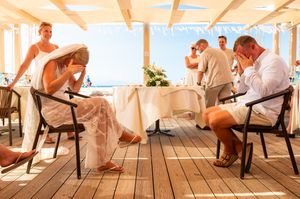 Guests in white attire relax at an open-air beachside venue with wooden floors during a sunny outdoor wedding.