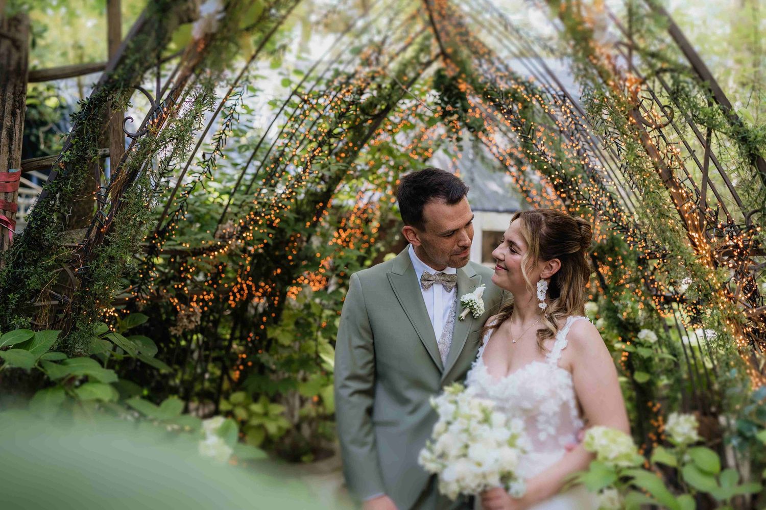 Romantic wedding portrait under garden archway decorated with twinkle lights.