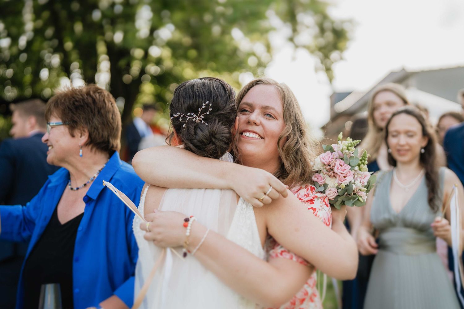 Joyful wedding celebration moment as attendees share warm embraces outdoors.