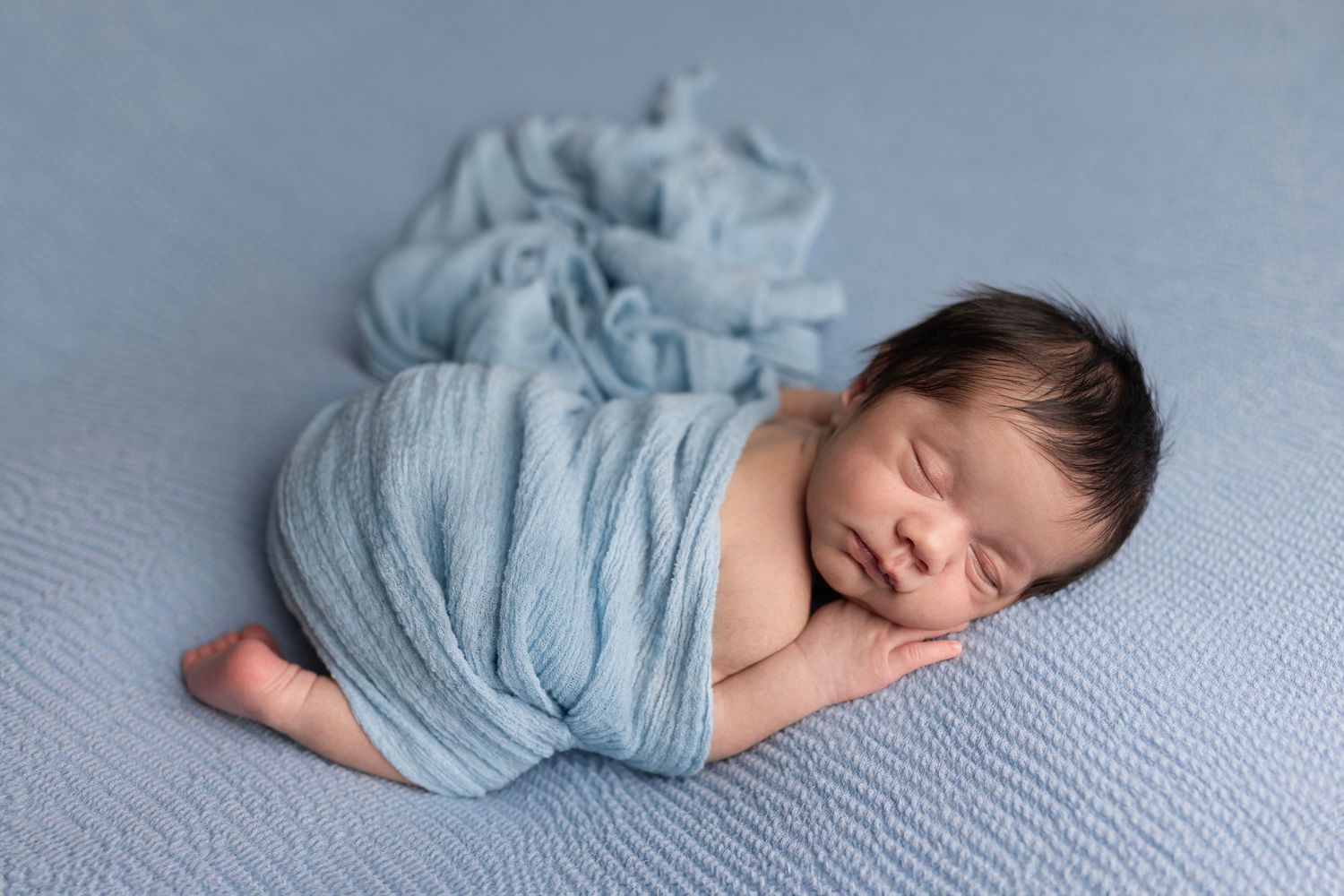 Newborn baby boy poses for newborn photos studio Elizabeth Lang Photography Surrey Cloverdale. On blue and wrapped in a blue blanket