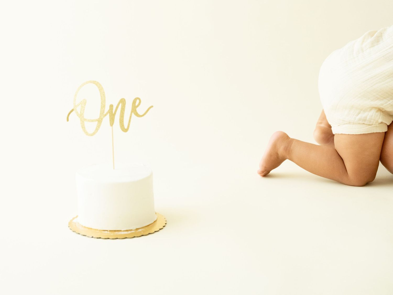 A white wedding cake sits on a plain backdrop with delicate frosting details and edible pearls.