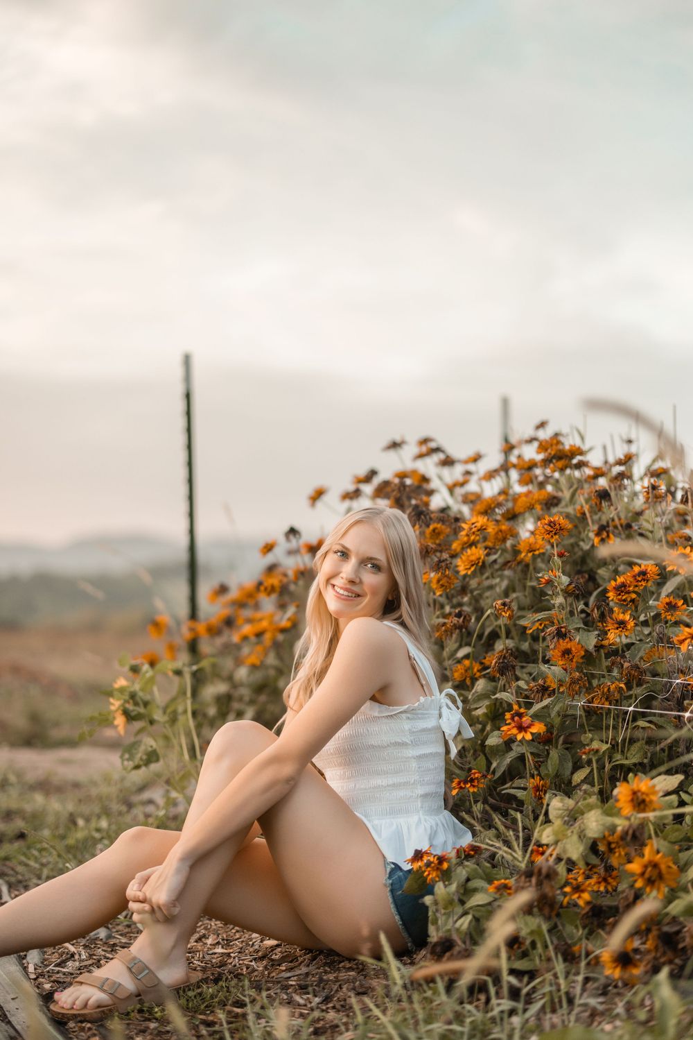 Someone sits among vibrant orange wildflowers in a white dress during golden hour in a rural field setting.