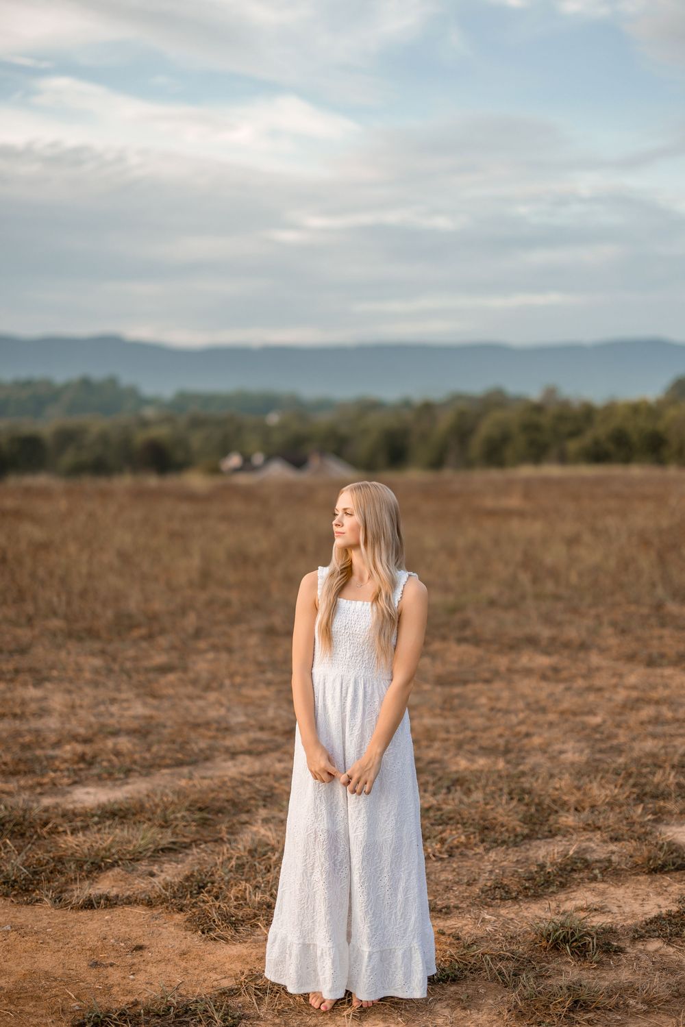 A long white dress contrasts beautifully against a golden field with misty mountains in the background.
