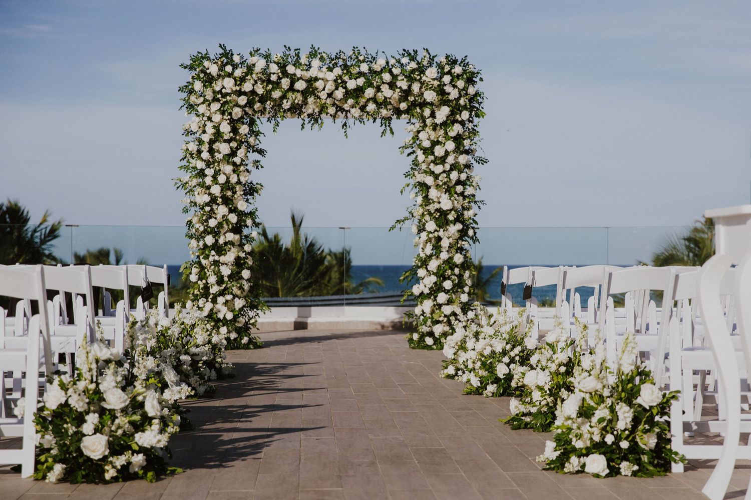 Beautiful white floral arch and chairs set up for beach wedding ceremony.