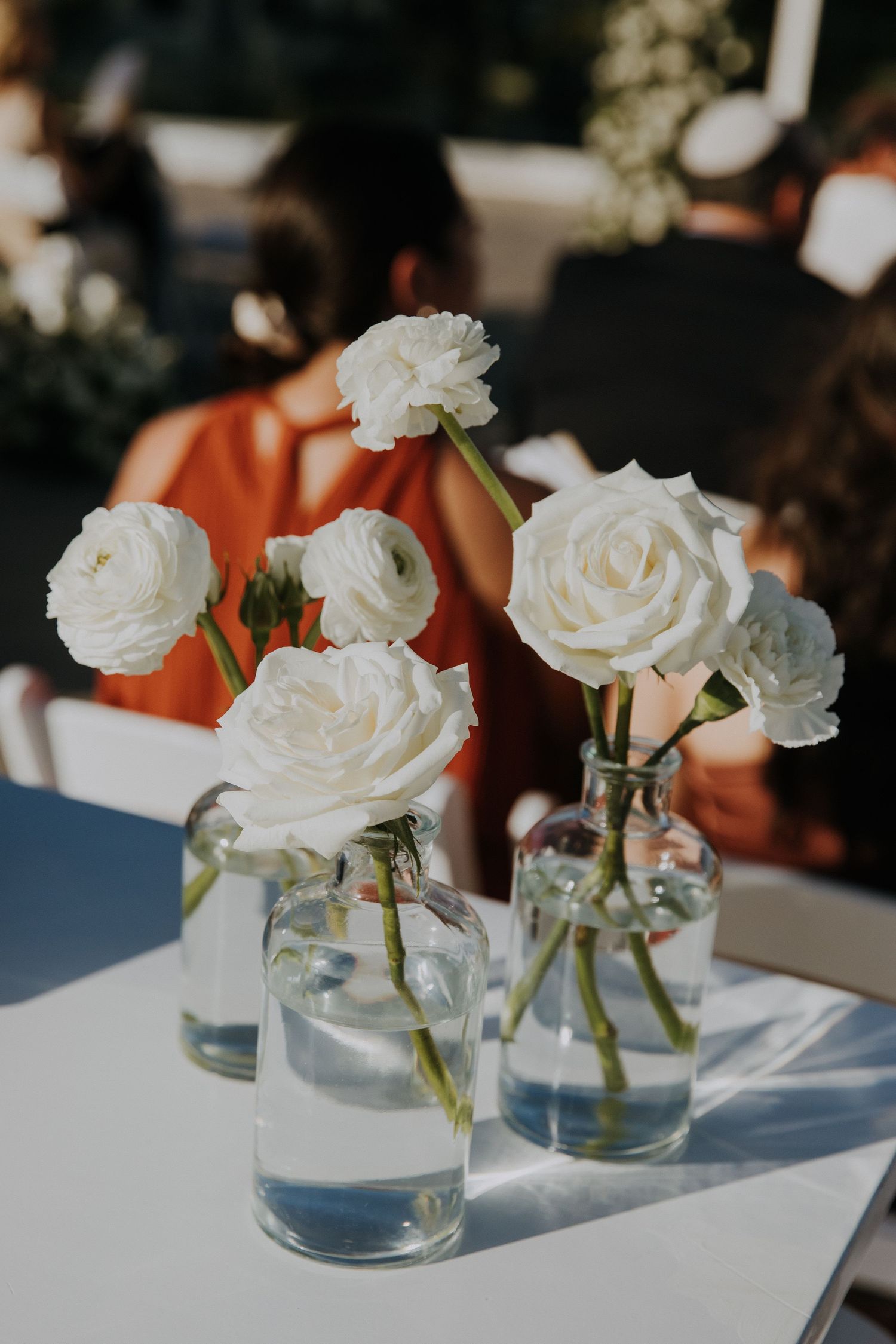 Elegant white roses arranged in clear glass vases on wedding reception table.