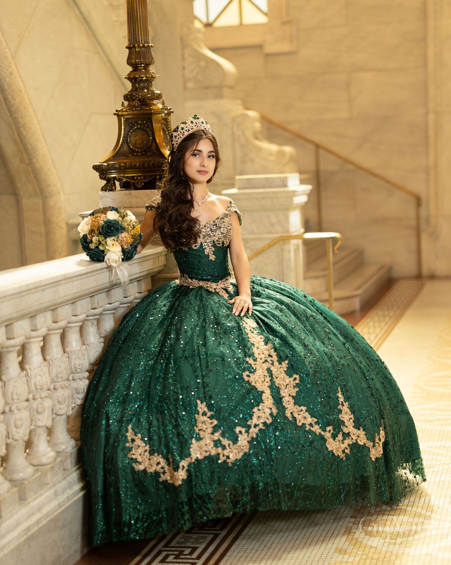 An elaborate emerald green ballgown with gold accents sparkles on a grand marble staircase in warm lighting.