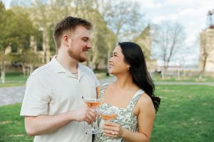 A couple shares a joyful moment together while holding glasses in a sunny park setting.