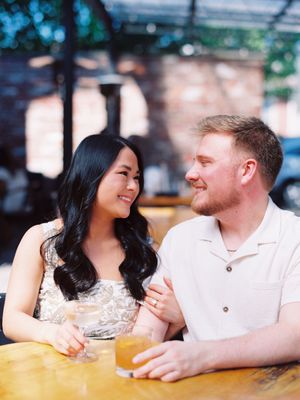 A couple shares a romantic moment at an outdoor cafe as they lean in close together and smile warmly at each other.