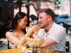 A romantic couple shares french fries while dining at a restaurant and laughing together.
