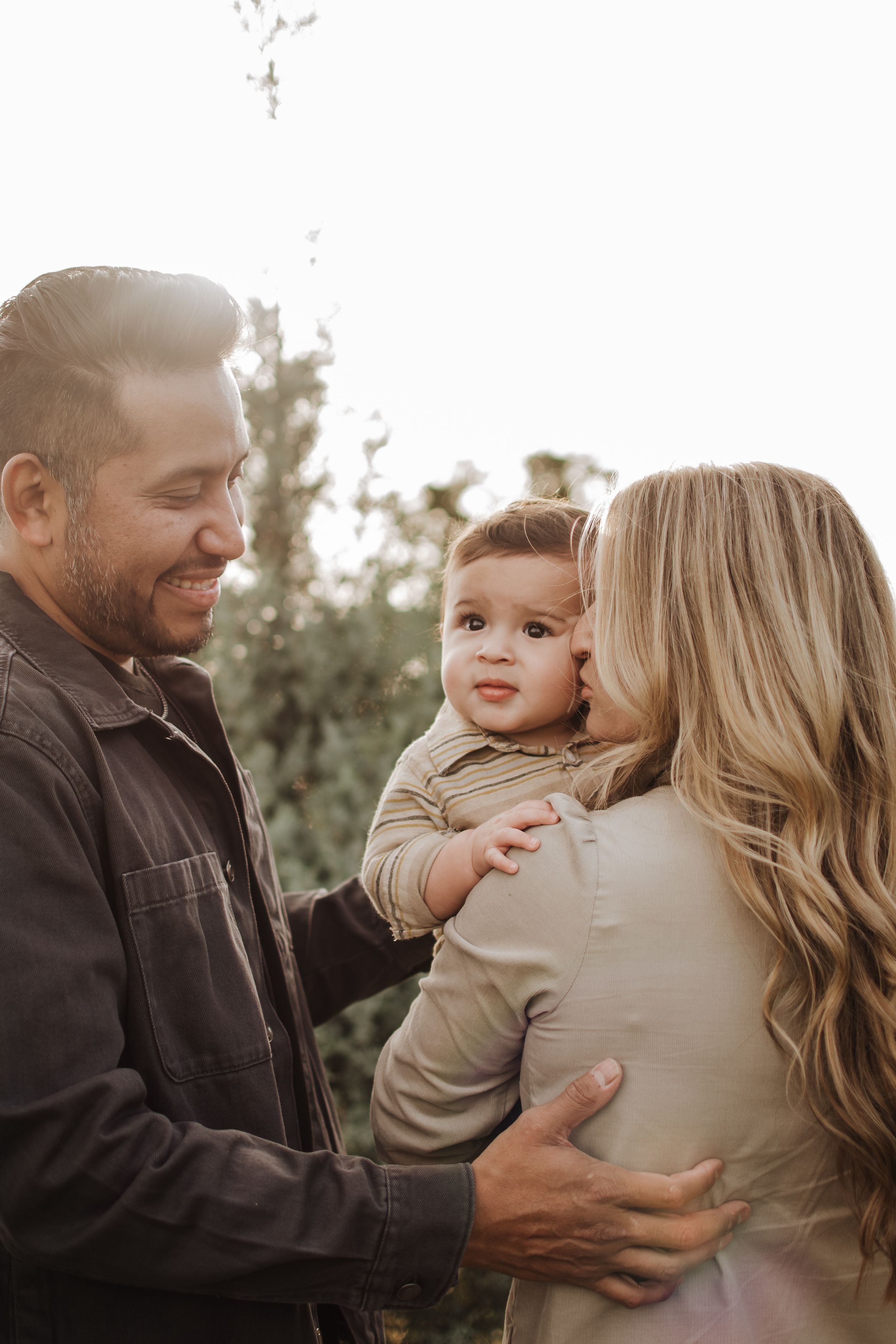 Intimate family portrait showing tender moments between parents and their baby in an outdoor setting. Haynie Green Acres Farm