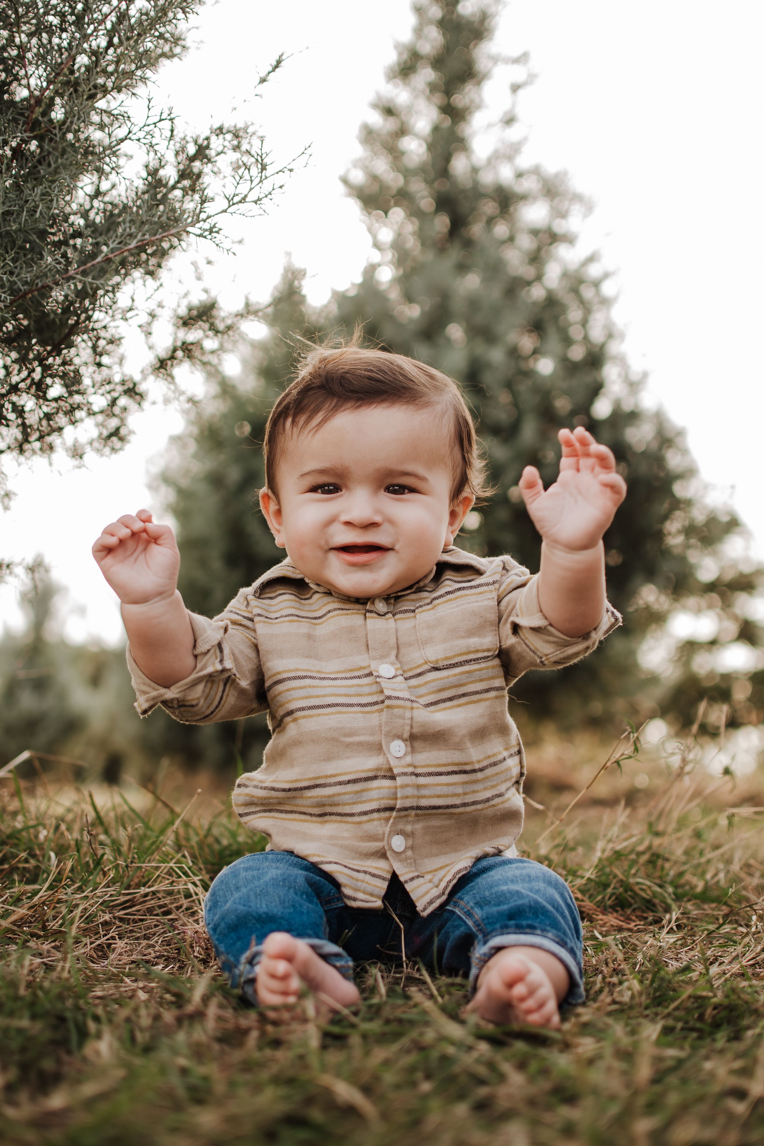 Happy baby in tan shirt and jeans sitting on grass with raised arms. Haynie Green Acres Farm