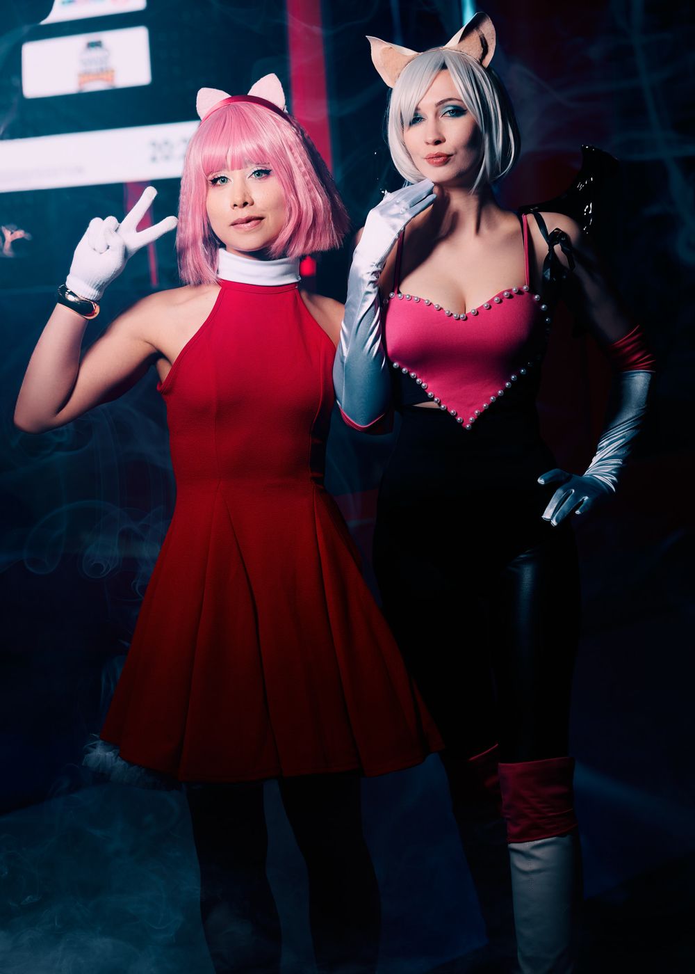A cosplay duo in contrasting red and black outfits strike dynamic poses against a dark backdrop.