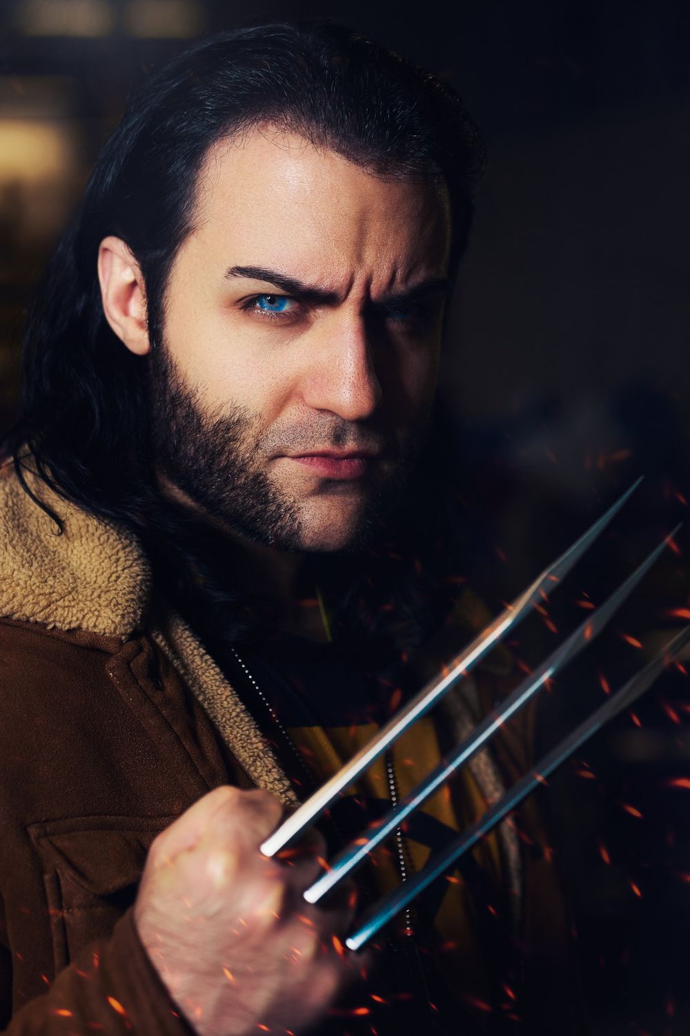 Dark moody cosplay portrait of Wolverine with metal claws in brown leather jacket and facial hair.