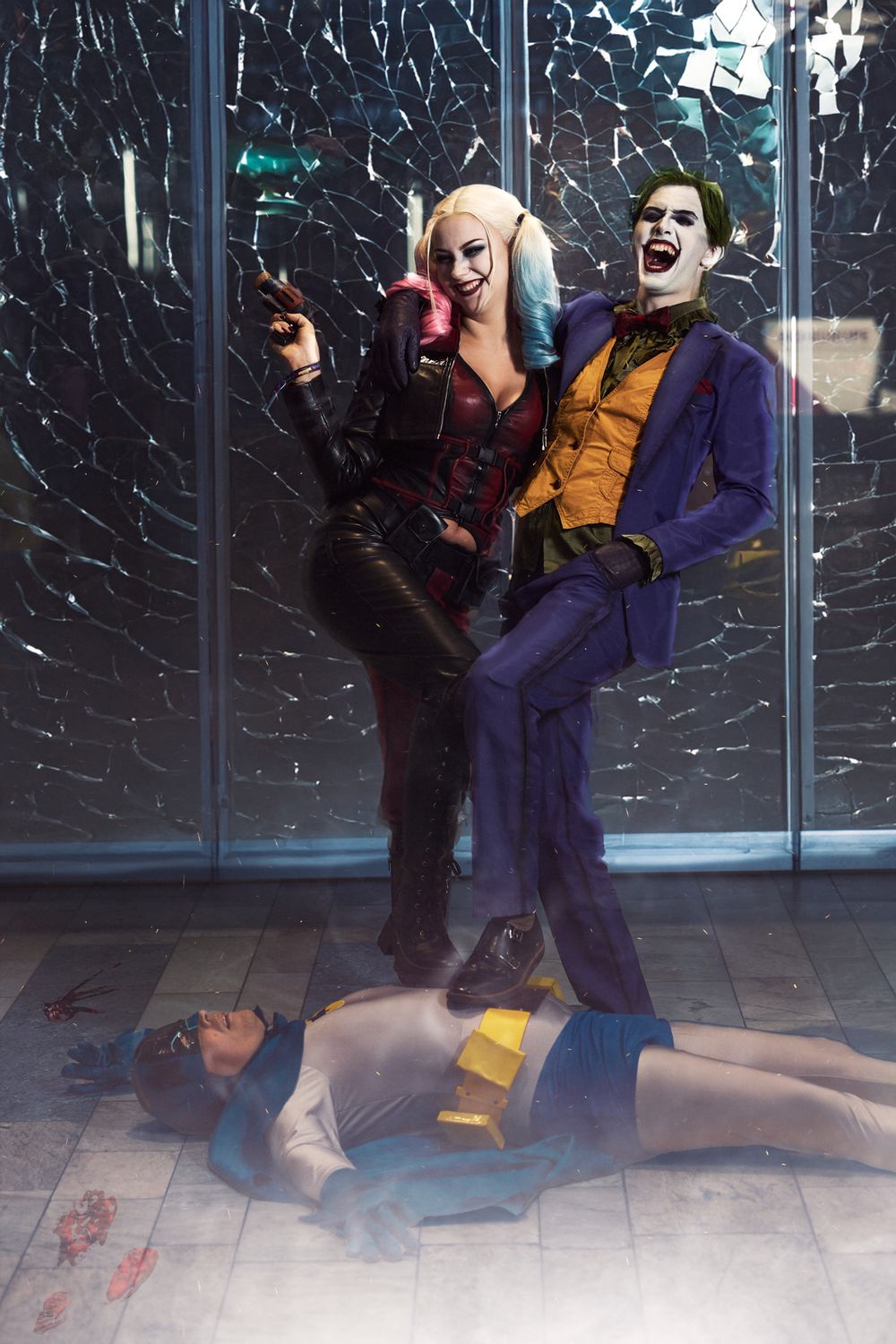 Dark cosplay scene depicting two villainous characters in purple and black costumes posing dramatically with a fallen figure.