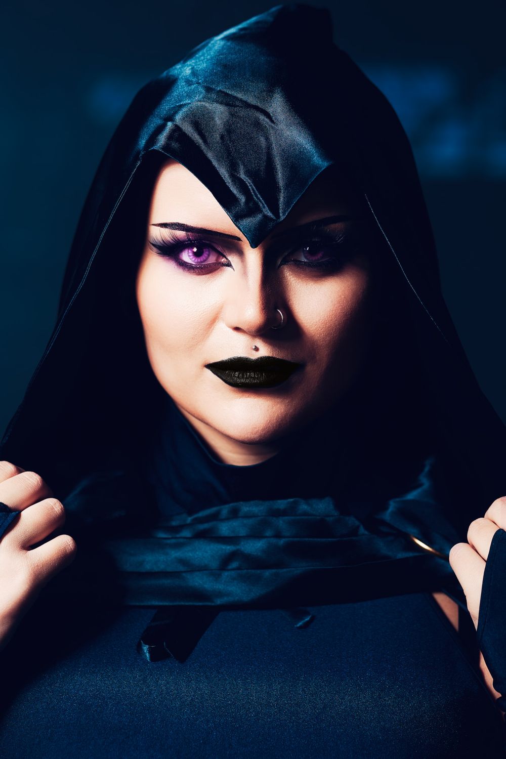 Dark fantasy portrait with black hooded figure and dramatic violet eyes against moody blue background.