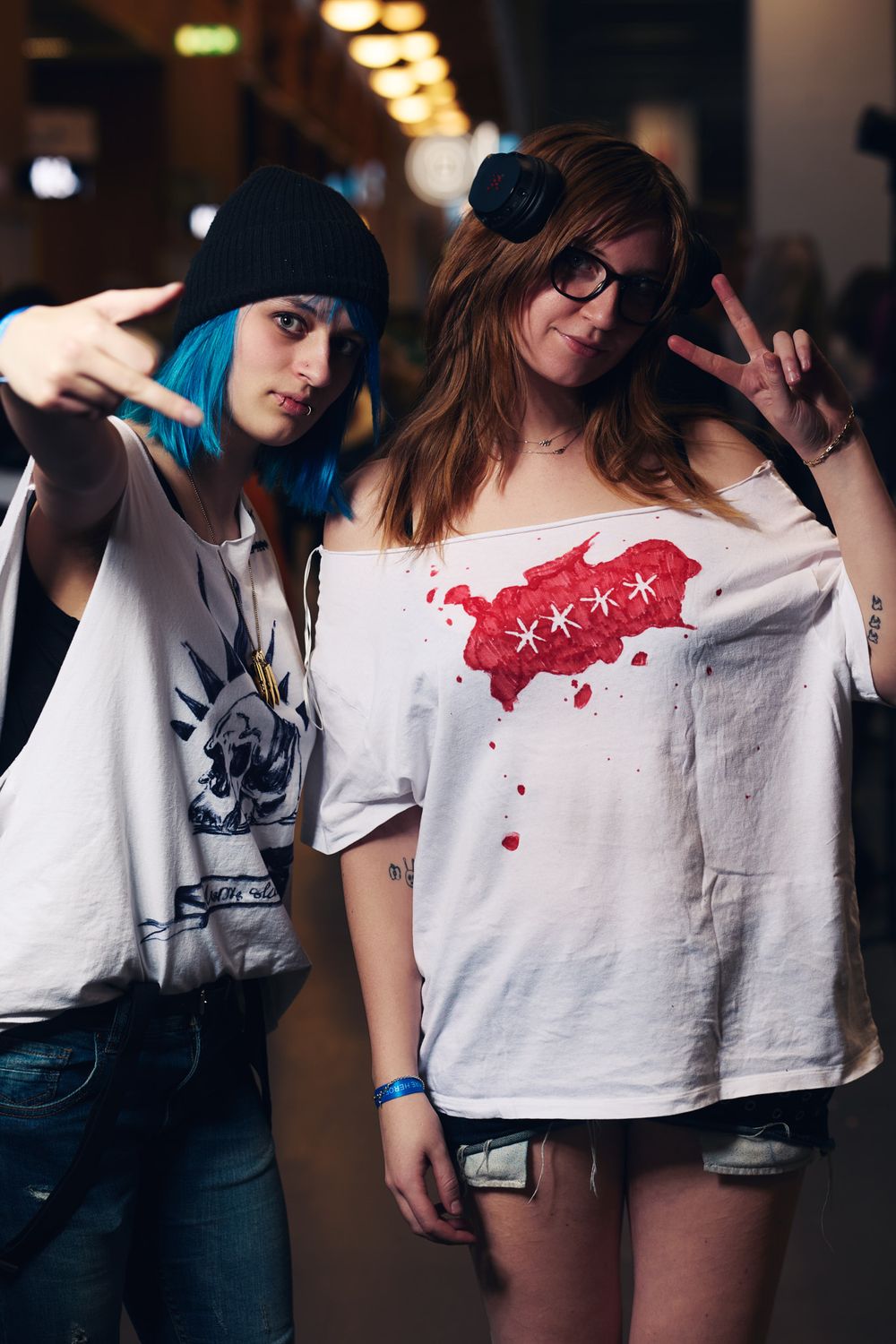 Two people posing playfully in casual outfits, with one wearing a beanie and blue hair and another in a red graphic t-shirt.
