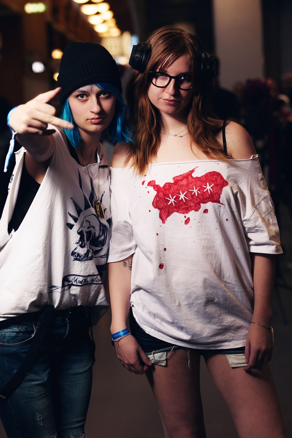 Two young people pose together wearing casual t-shirts, one in a beanie and headphones, the other in glasses.