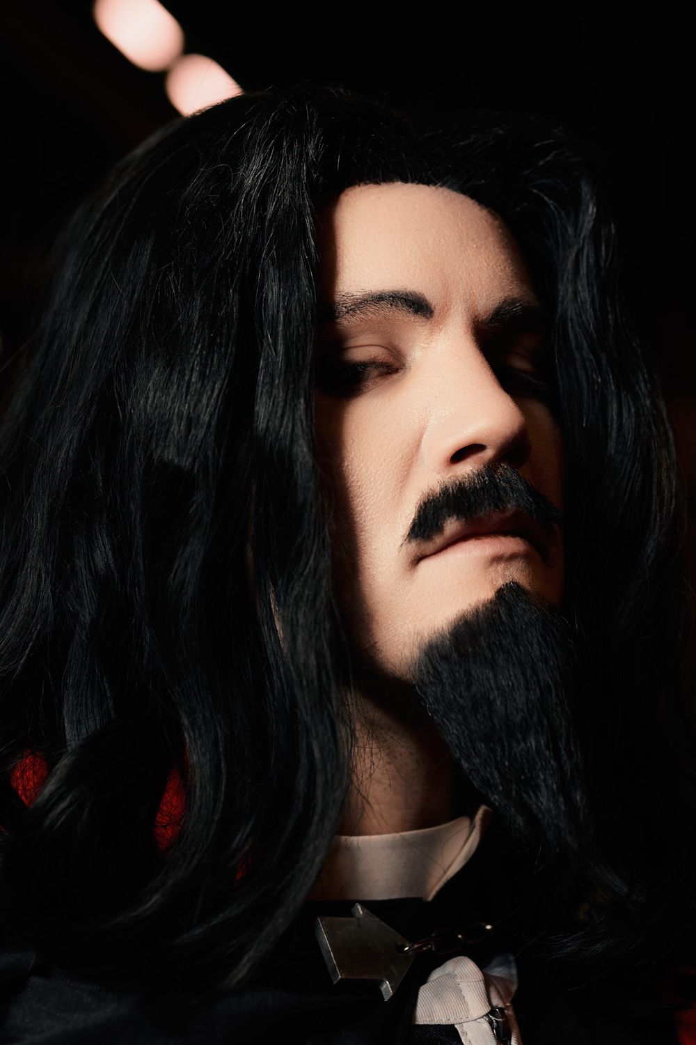 A close-up portrait of a person with long black hair, mustache, beard, and formal attire with a bowtie.