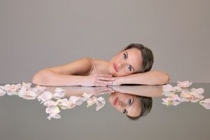 Minimalist portrait with scattered pink flower petals creating romantic composition on light background.