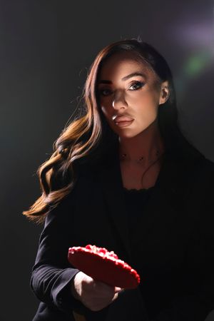 Dramatic side profile portrait in shadows with long wavy hair and red lipstick against dark background.